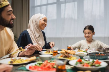 Gülümseyen Orta Doğulu aile evde ramazan yemeği yerken konuşuyor. 