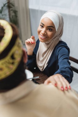 tesettürlü gülümseyen Afrikalı Amerikalı kadın evde bulanık kocaya bakıyor. 