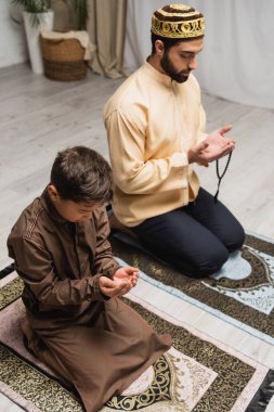 Middle eastern father and son praying during salah at home 