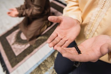 Dua boncuklarıyla evdeki bulanık oğlunun yanında dua eden adamın kısmi görüntüsü 