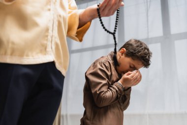 Muslim boy holding hands near face while praying with father at home 