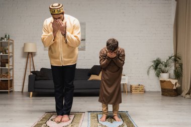 Barefoot muslim father and boy praying on rugs at home 
