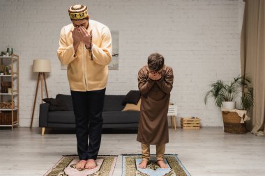 Çıplak ayaklı müslüman baba ve çocuk evde kilim üzerinde dua ediyorlar. 
