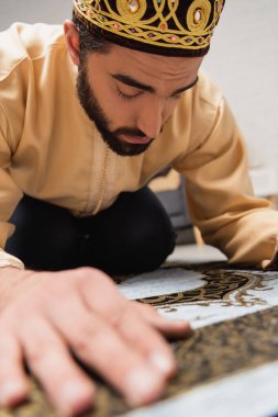 Young muslim man praying on rug during ramadan at home 