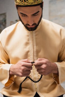 Young muslim man praying and holding prayer beads at home 