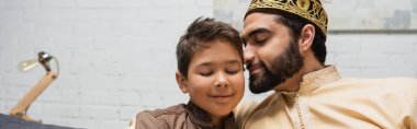 Muslim father smiling near preteen son at home, banner  clipart