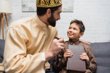 Müslüman baba evde Kuran 'ı elinde tutan oğluyla konuşuyor. 