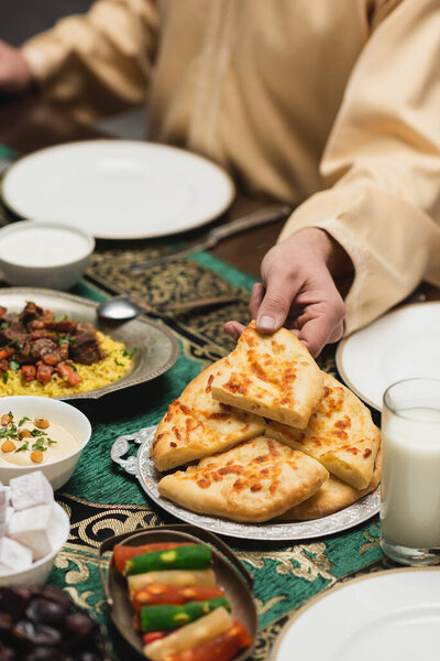 Cropped view of muslim man taking pita bread near food during ramadan dinner 
