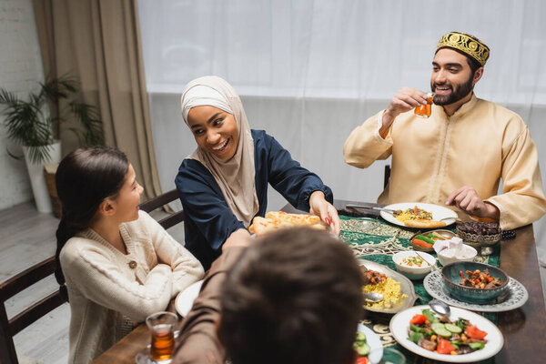 African american mother in hijab holding pita bread near family during ramadan 