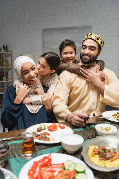 Cheerful middle eastern family hugging near food during ramadan at home 