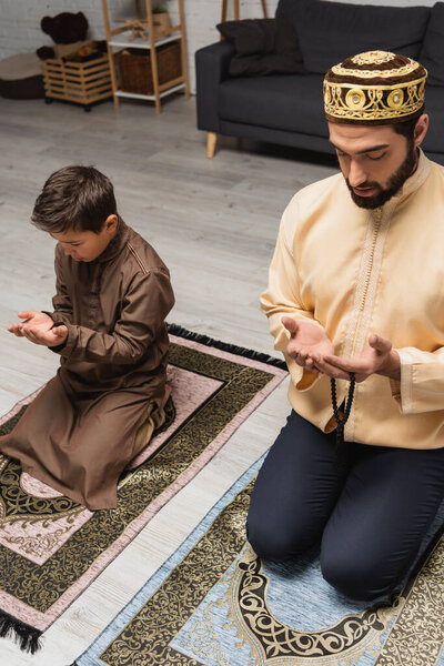 Muslim father with prayer beads praying near son at home 