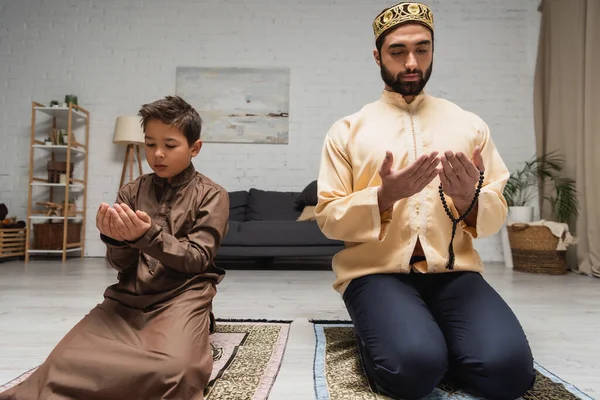 Muslim man and son praying on rugs during ramadan at home
