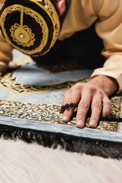 Blurred muslim man with prayer beads praying on carpet at home 