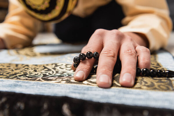 Размытый ближневосточный мужчина с четками для молитвы, молящийся дома. 