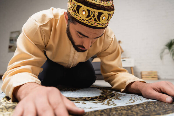 Young muslim man doing salah on rug at home 
