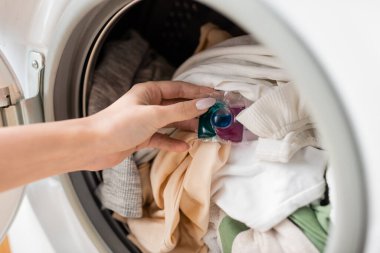 Cropped view of woman putting detergent pod on clothes in washing machine 