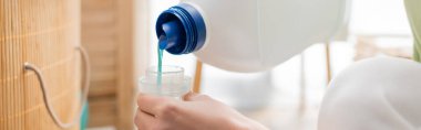 Cropped view of woman pouring softener in laundry room, banner 