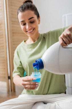 Smiling woman pouring liquid washing powder in laundry room 