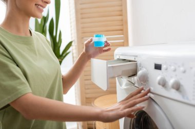 Cropped view of smiling woman holding liquid cleaner near washing machine at home 