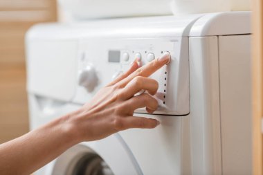 Çamaşır odasında beyaz çamaşır makinesini akort eden kadın manzarası. 