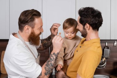 happy gay fathers holding daughter and barrette in kitchen  clipart