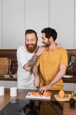 Neşeli eşcinsel adam evde yemek pişirirken mutlu eşe sarılıyor. 