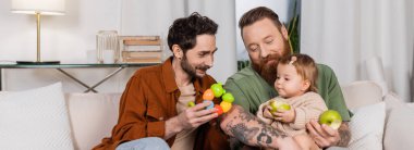 Kızının yanında oyuncak tutan gülümseyen gay adam ve elma, pankart 