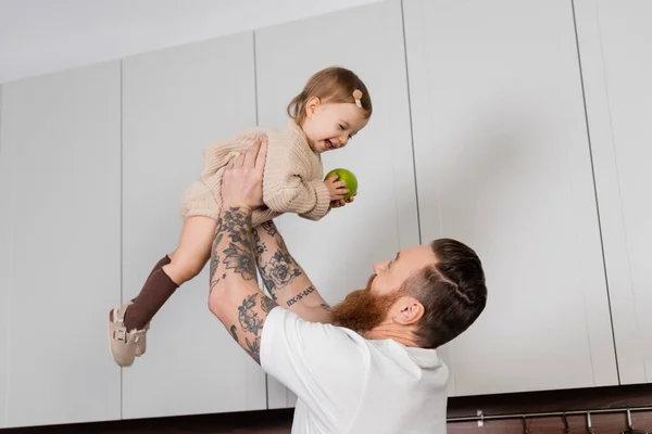 Dövmeli Adam Yeni Yürümeye Başlayan Kızını Mutfakta Elmayla Tutuyor — Stok fotoğraf
