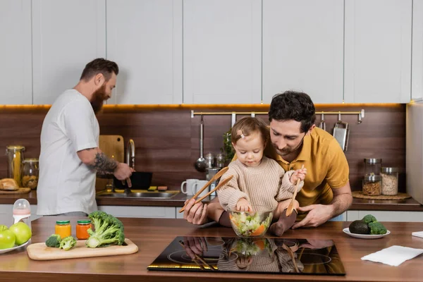 Homosexuali Care Țin Fiica Copilului Lingură Lângă Salată Proaspătă Bucătărie — Fotografie, imagine de stoc