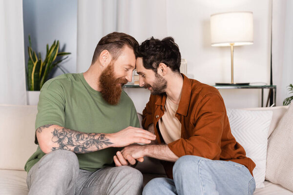 Side view of same sex couple holding hands on couch at home 