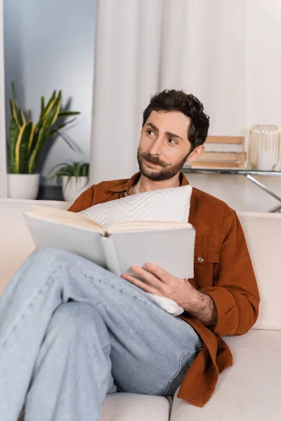 Bearded Man Holding Pillow Book Couch Home — Foto de Stock