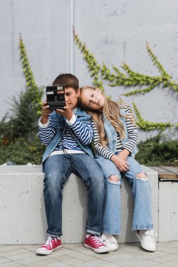 Şık giyinmiş çocuk kot ve kot giyen kızın yanında fotoğraf çekiyor. 