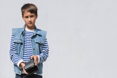 İyi giyimli, kot giyen, gri arka planda klasik fotoğraf makinesi olan bir çocuk.  