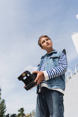 İyi giyimli, kot elbiseli, klasik fotoğraf makinesi olan bir gencin alçak açılı görüntüsü. 