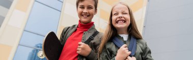 happy preteen boy holding penny board while standing with girl near mall, banner 