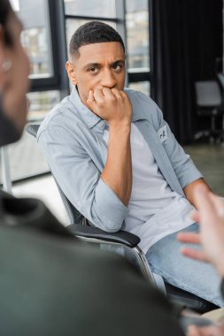 Worried african american man with alcohol addiction listening story during therapy in rehab center  clipart