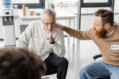 Man calming mature person with alcohol addiction during group therapy session in rehab center  clipart