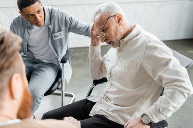 Alkol bağımlısı hoşnutsuz bir adam rehabilitasyon merkezinde ırklar arası insanların yanında oturuyor. 