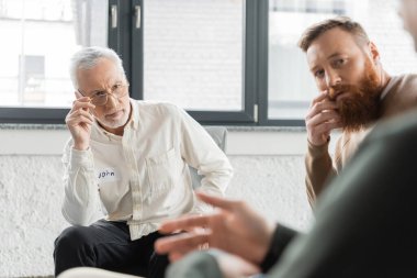 People looking at blurred man during alcoholics meeting in rehab center  clipart