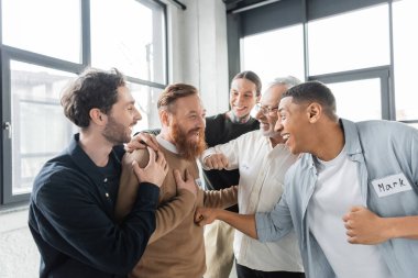 Interracial people hugging cheerful man during alcoholics meeting in rehab center  clipart