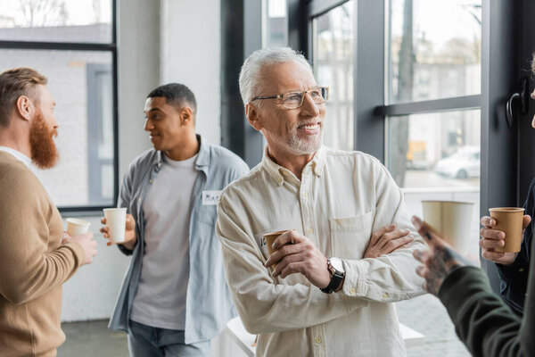 Smiling mature man holding paper cup during alcoholics meeting in recovery center 