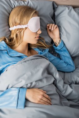 Maskeli sarışın bir kadın ve yatakta dinlenen ipek bir pijama. 