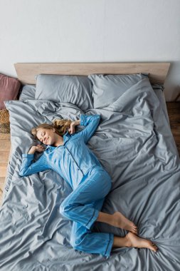 Çıplak ayaklı ve mavi pijamalı neşeli bir kadın yatağında yatıyor. 