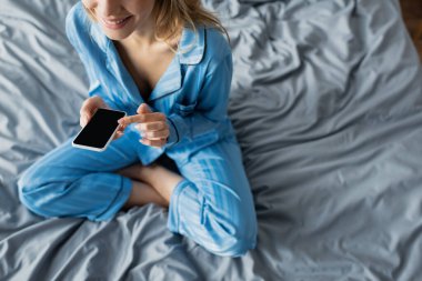 Mavi pijamalı, beyaz ekranlı akıllı telefon kullanan gülümseyen kadın manzarası. 
