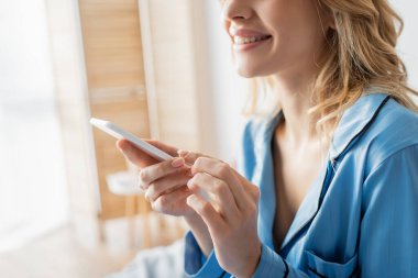 Evde akıllı telefon kullanan pijamalı neşeli kadın manzarası. 