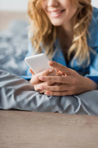 cropped view of cheerful woman chatting on smartphone while lying on bed in modern apartment