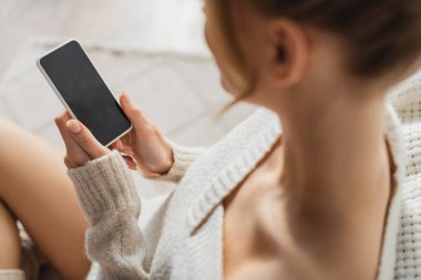 Beyaz ekran ile akıllı telefon kullanan rahat kazaklı sarışın kadının yukarıdan görünüşü 