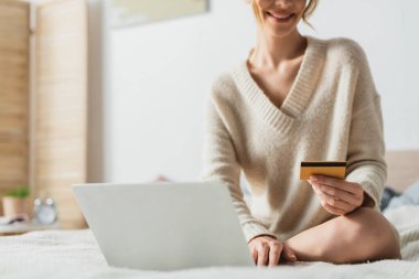 Yatak odasında online alışveriş yaparken kredi kartı tutan mutlu kadının kısmi görüntüsü 