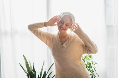 Modern apartmanda müzik dinleyen, kablosuz kulaklıklı mutlu genç bir kadın. 