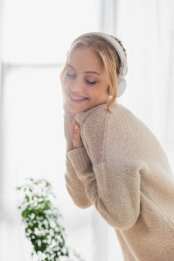 Evde eğlenirken kablosuz kulaklıkla müzik dinleyen genç bir kadın. 